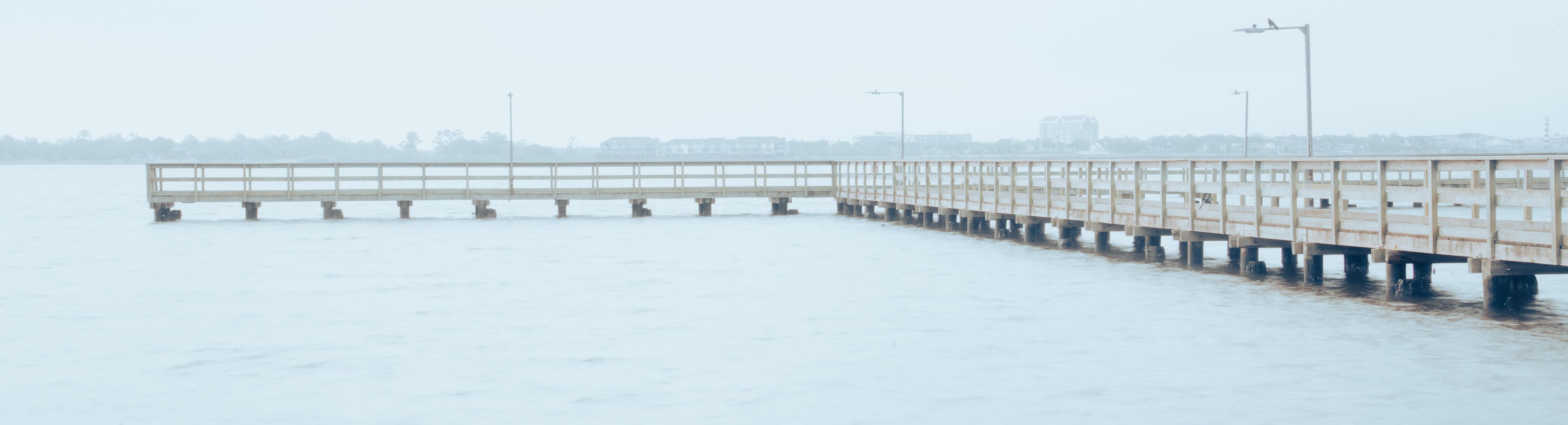 A wooden pier extending into a foggy body of water with a cityscape in the background.