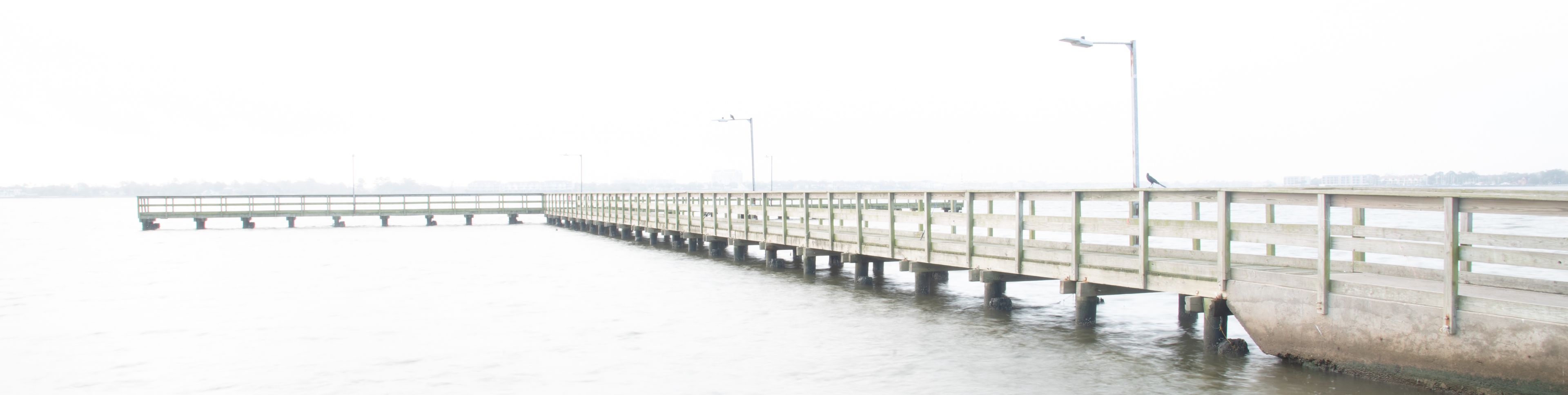 A long, narrow concrete pier extending into a body of water, supported by multiple pillars.