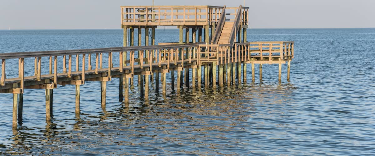 Wooden fishing piers stretching out over Galveston Bay in Kemah, Texas, USA. Foot pier for saltwater fishing of vacation home/beach house rental/bay home in Lighthouse District waterfront at sunset