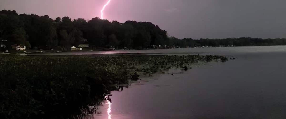 A stormy sky with a lightning strike over a body of water and a forested area.