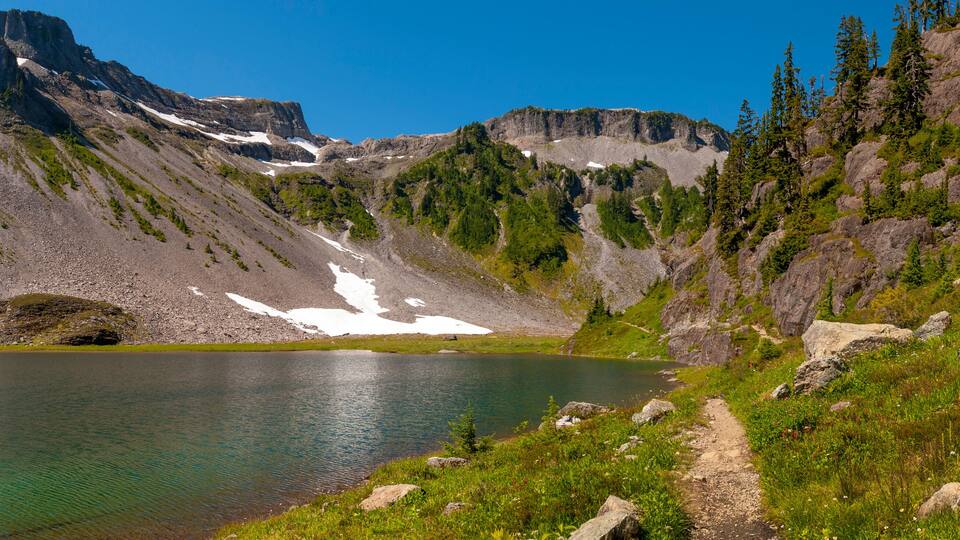 A mountain lake with a clear path leading to it, surrounded by rocky terrain and sparse vegetation.