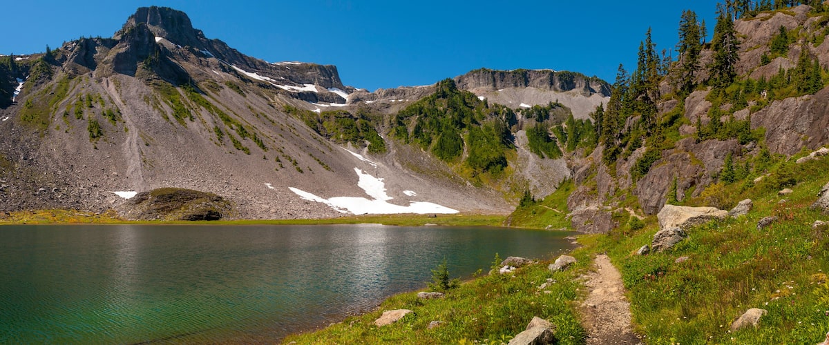 A mountain lake with a clear path leading to it, surrounded by rocky terrain and sparse vegetation.