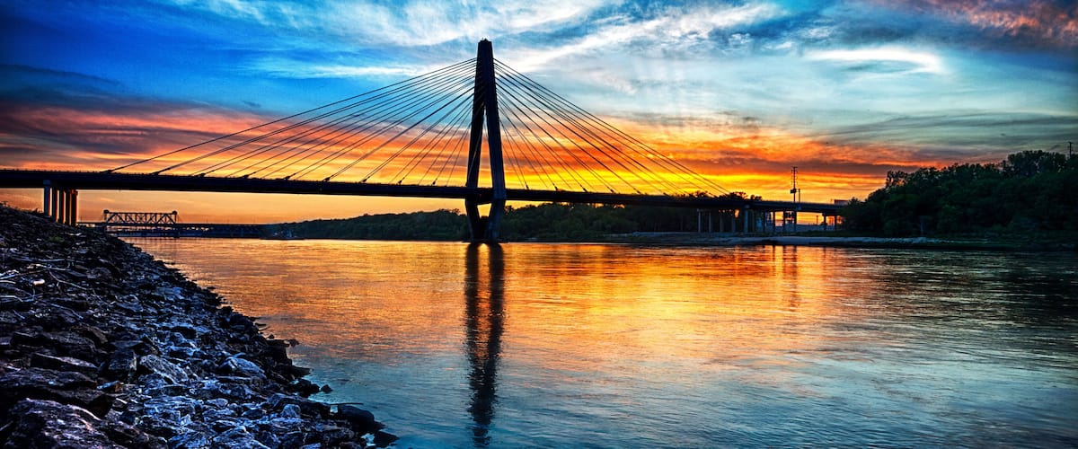 Un puente colgante al atardecer, con una costa rocosa.