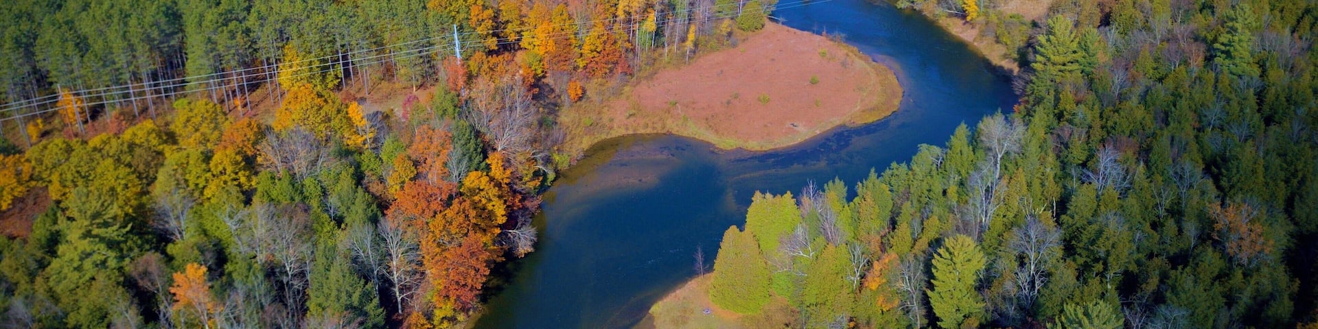An aerial view of a river winding through a forest with autumn foliage.