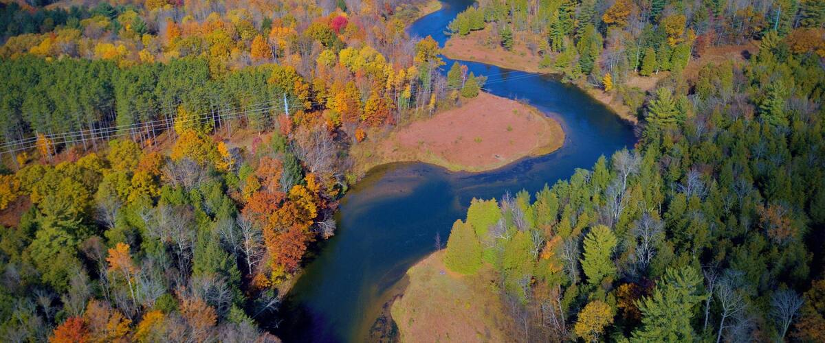 An aerial view of a river winding through a forest with autumn foliage.