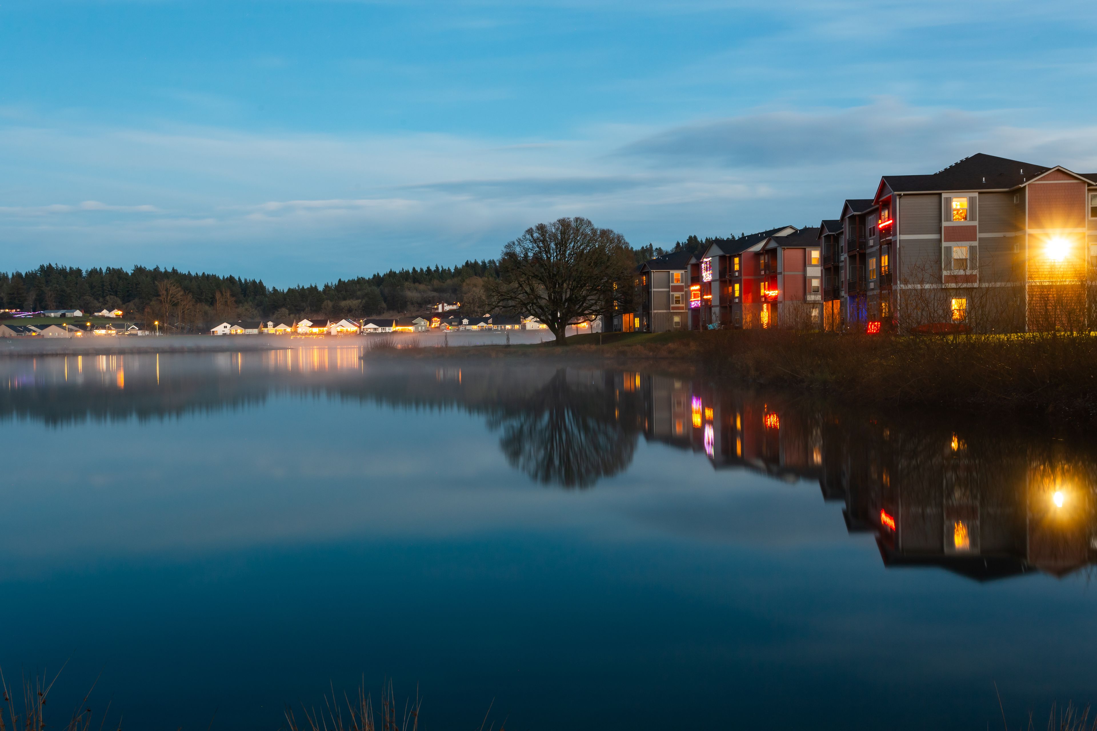 A calm lake reflecting buildings and trees.