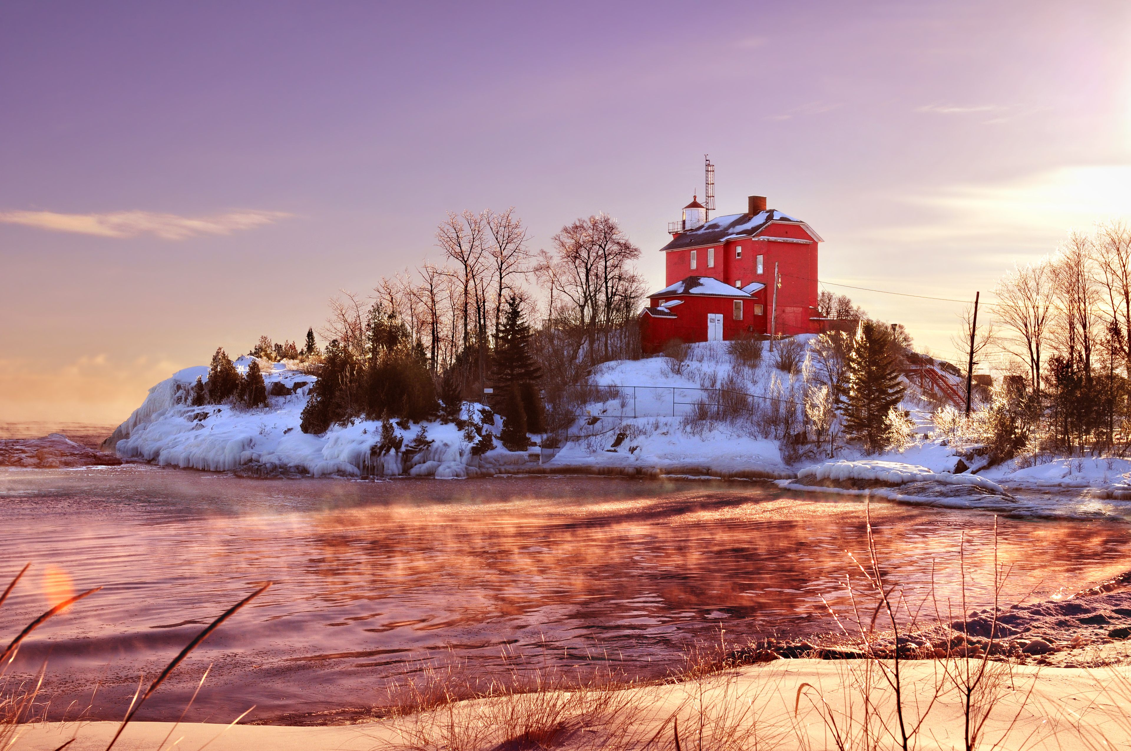 A red building on a snowy island with a frozen river in the foreground.