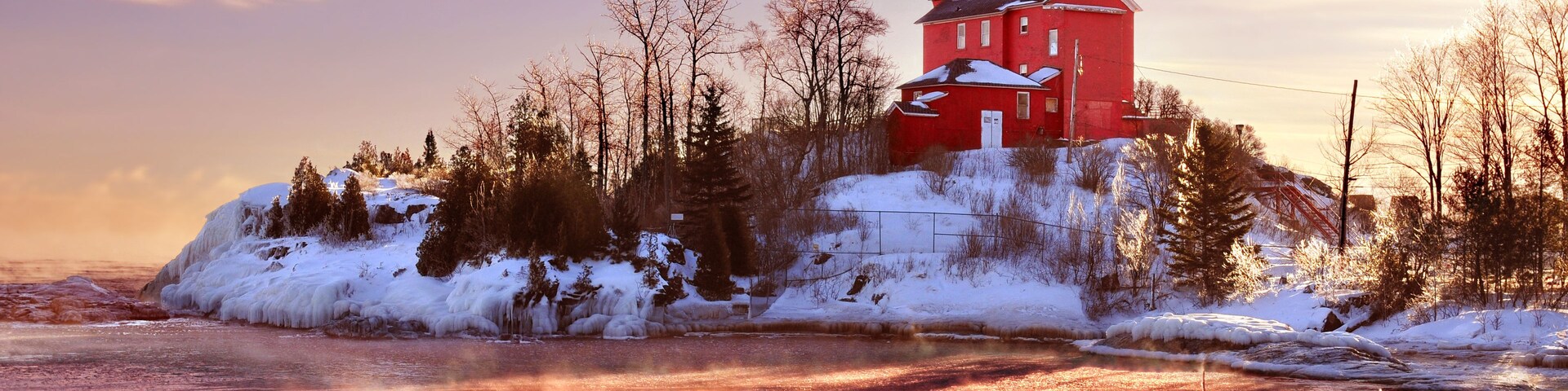 A red building on a snowy island with a frozen river in the foreground.