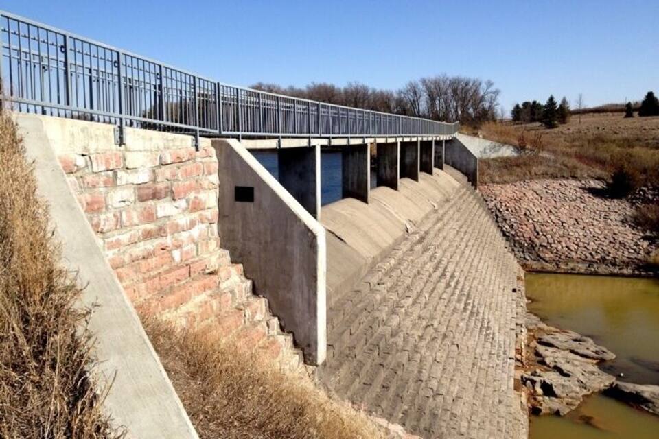Uma barragem de concreto com grades de metal e degraus que descem para um canal de água.