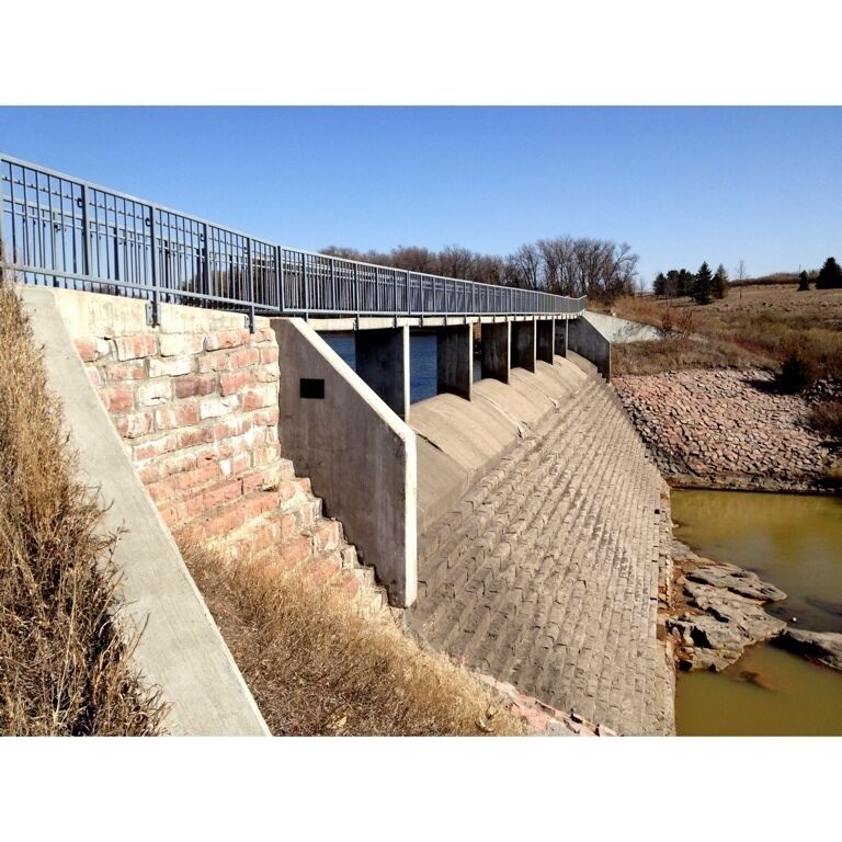A concrete dam with a metal railing and steps leading down to a water channel.