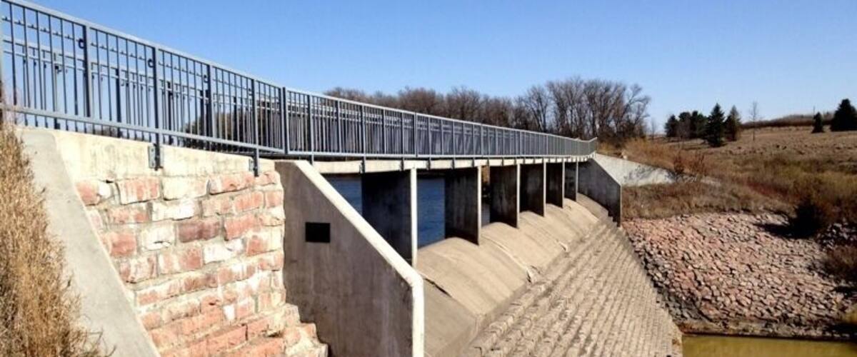 A concrete dam with a metal railing and steps leading down to a water channel.