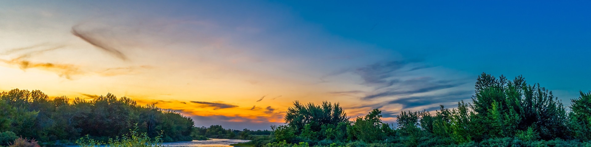 A river surrounded by dense forest during sunset.