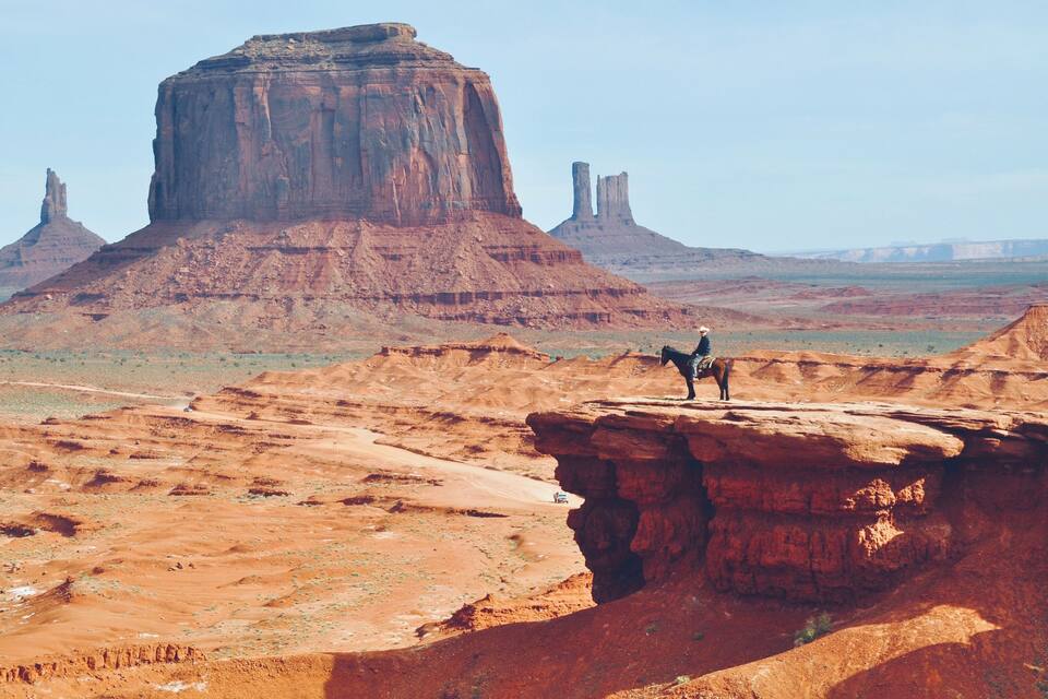 A person standing on a rock formation with a large mesa in the background.