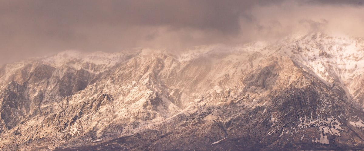 Snow-covered mountain peaks with rugged terrain and a cloudy sky.