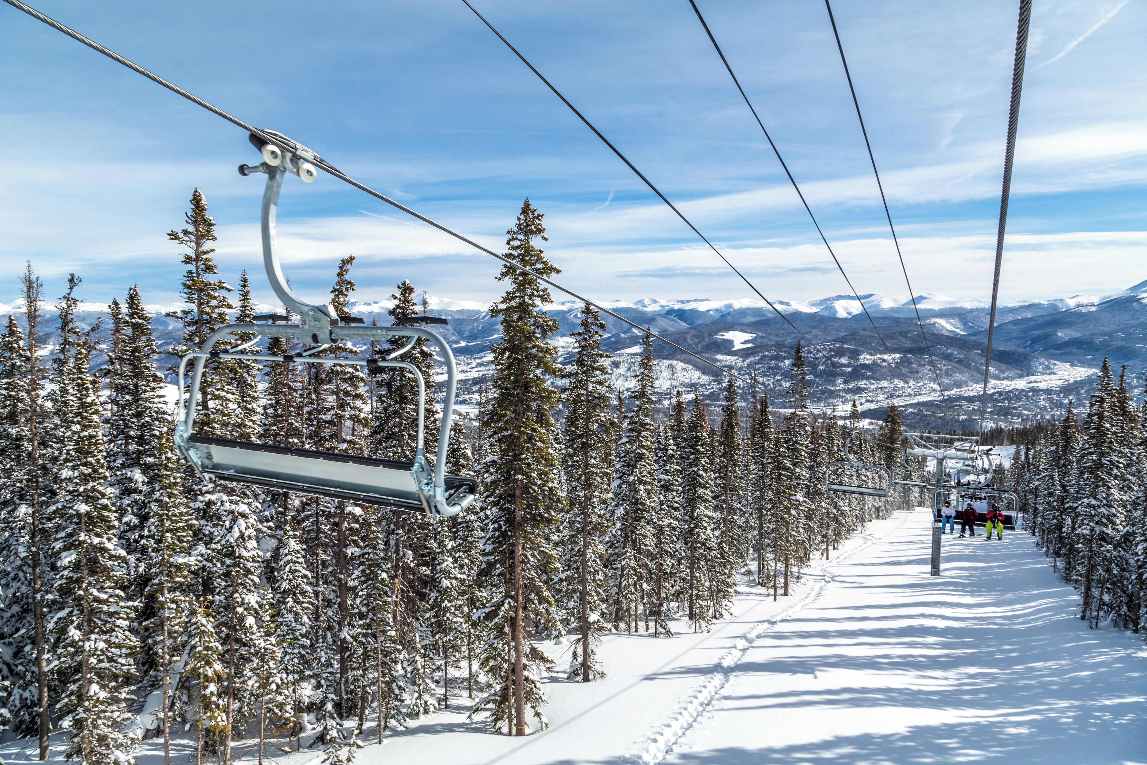 A ski lift with a snowy mountain landscape and evergreen trees in the background.
