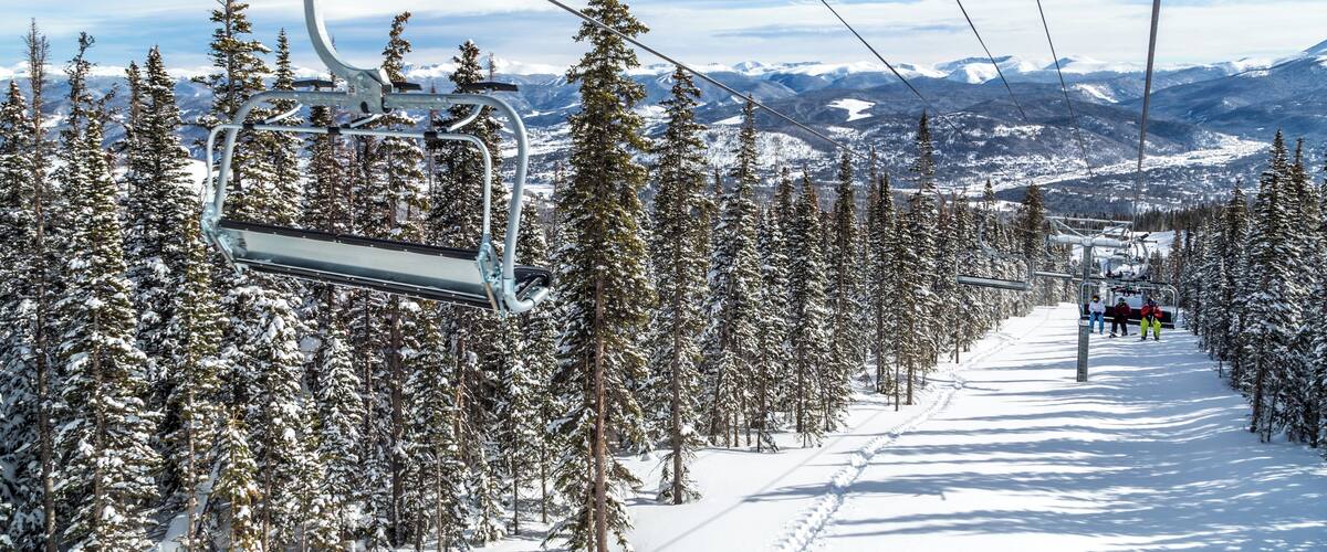 A ski lift with a snowy mountain landscape and evergreen trees in the background.