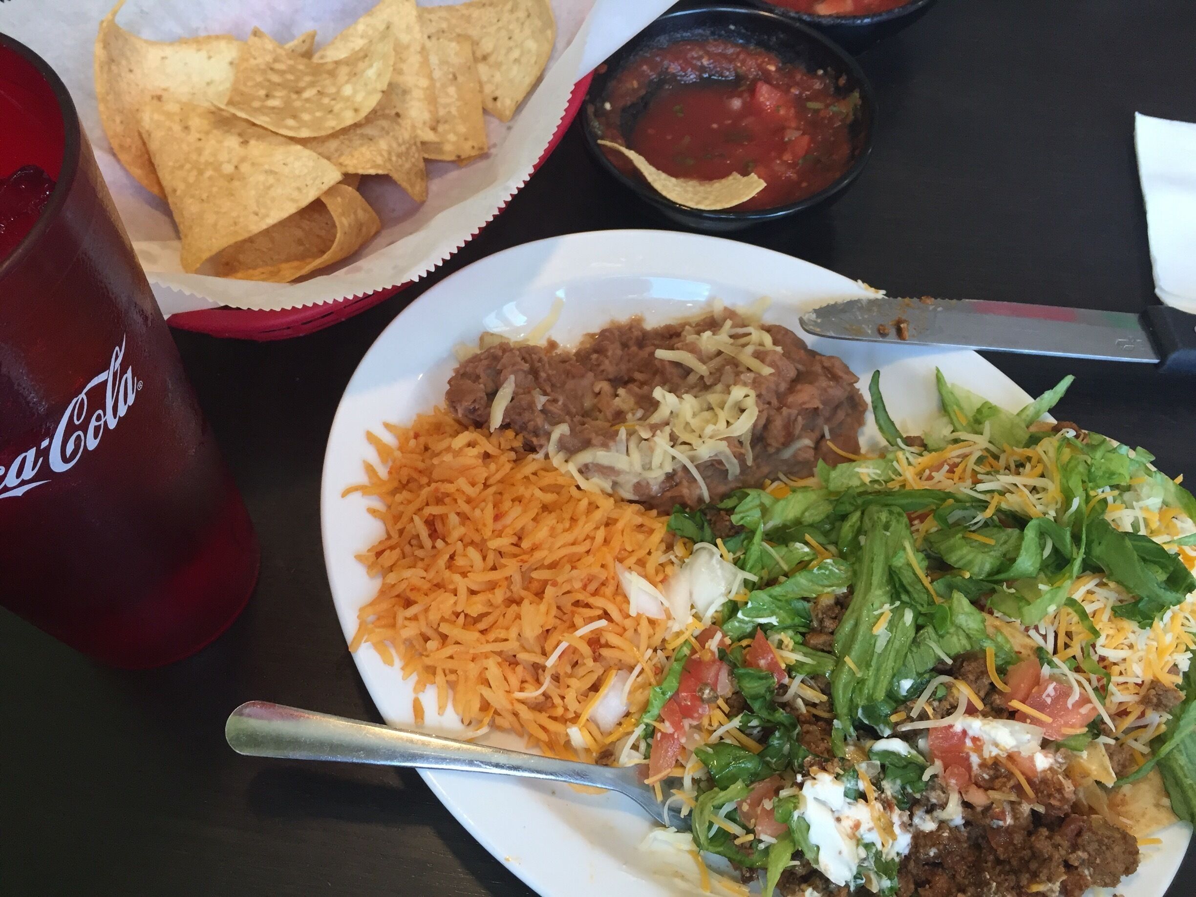 A plate of nachos, beans, rice, and a salad with cheese and lettuce.