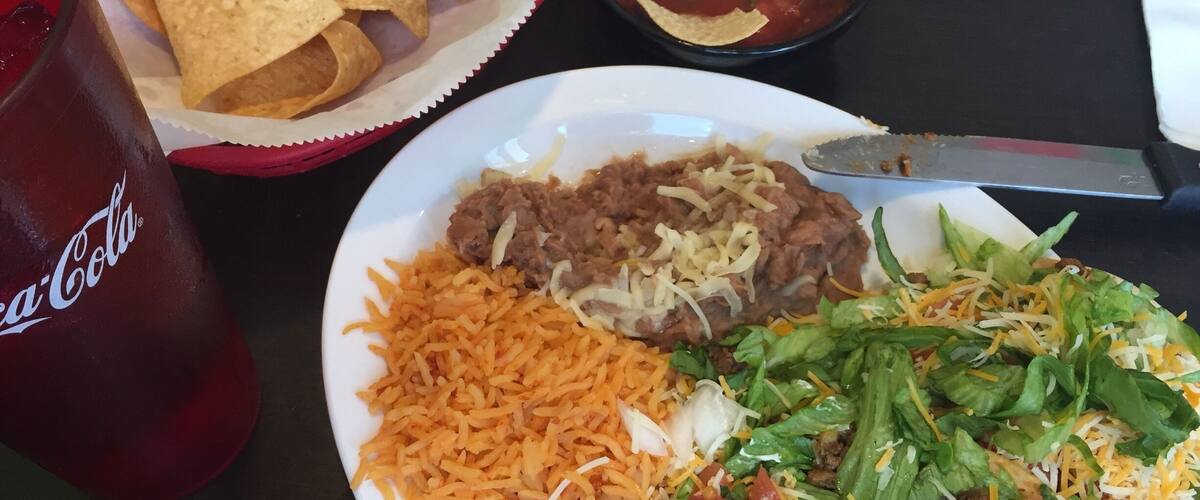 A plate of nachos, beans, rice, and a salad with cheese and lettuce.