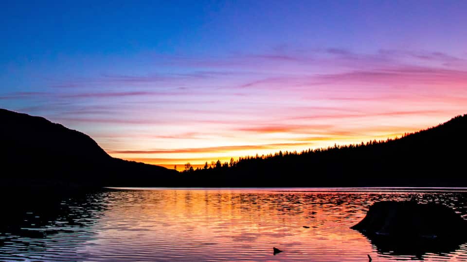 A sunset over a lake with mountains in the background.