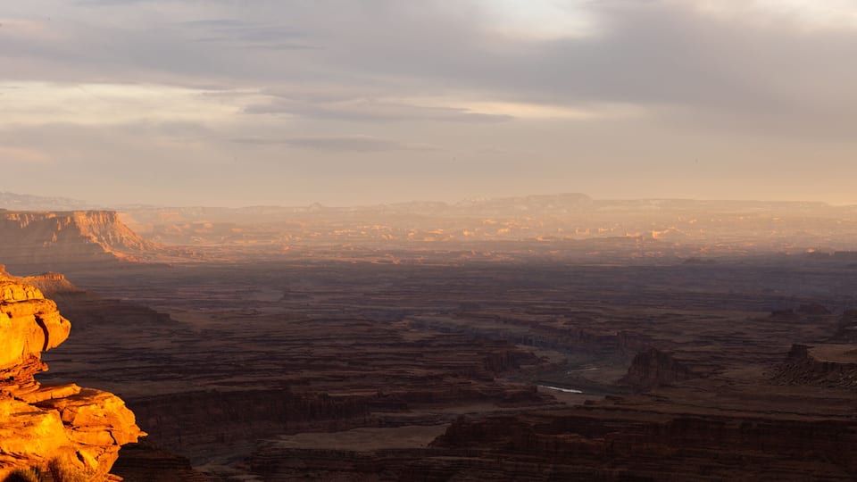 A canyon landscape with layered rock formations and a distant city skyline.
