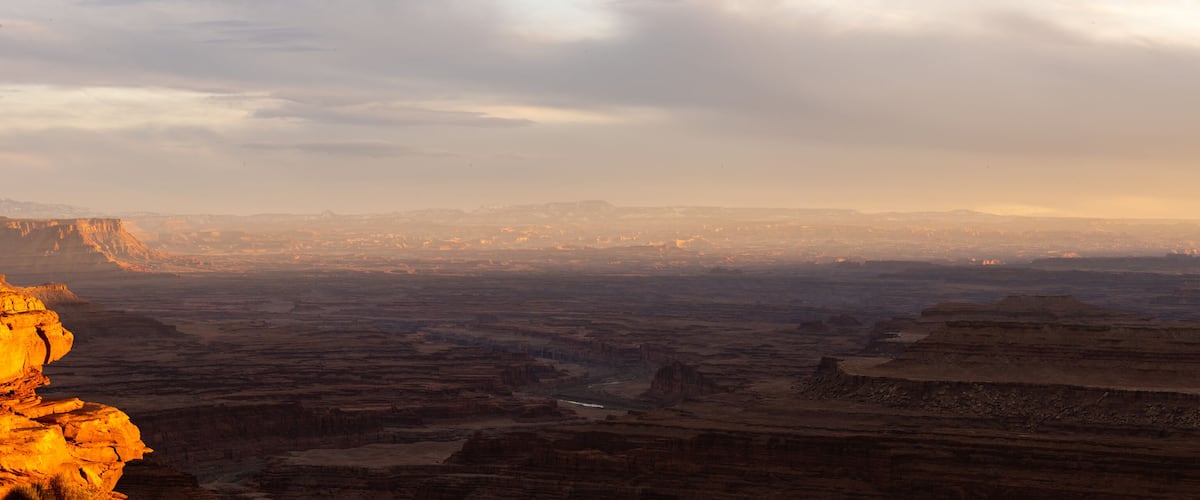 A canyon landscape with layered rock formations and a distant city skyline.