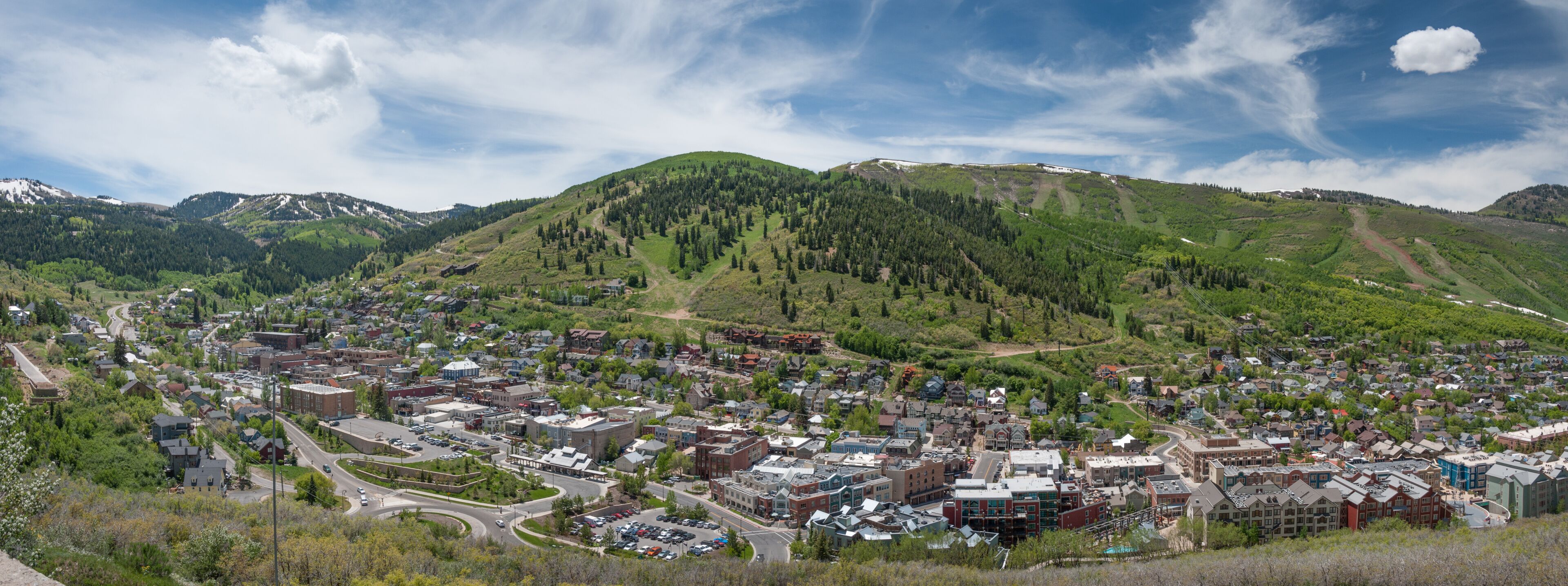 A town nestled in a valley with a backdrop of green hills and a mountain range.
