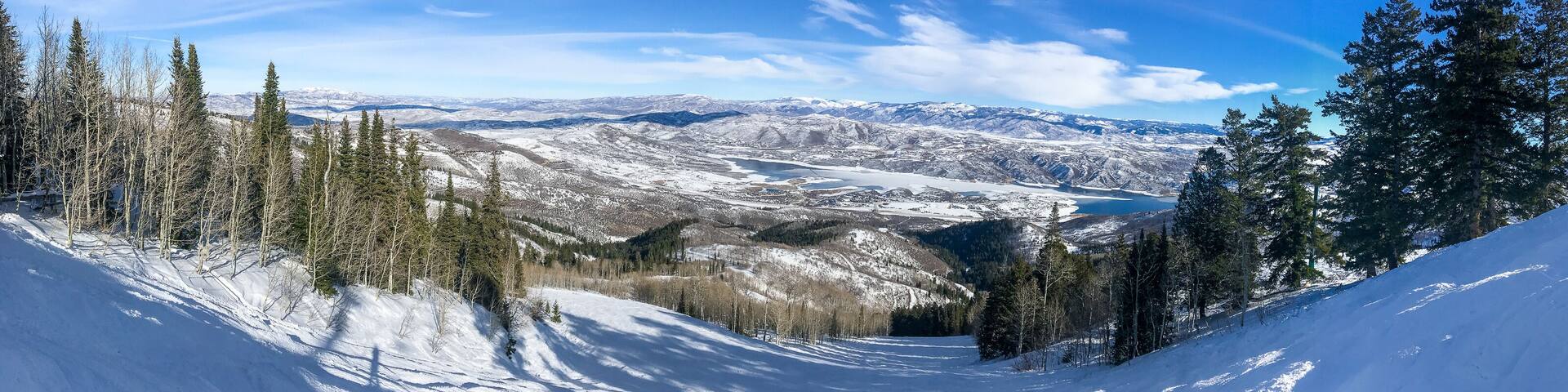 A snow-covered mountain landscape with a clear sky, a valley, and a lake.
