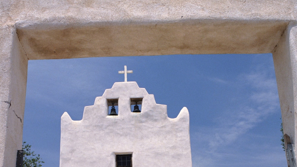 Eine weiße Kirche mit Kreuz, einem Glockenturm und einem Eingang.