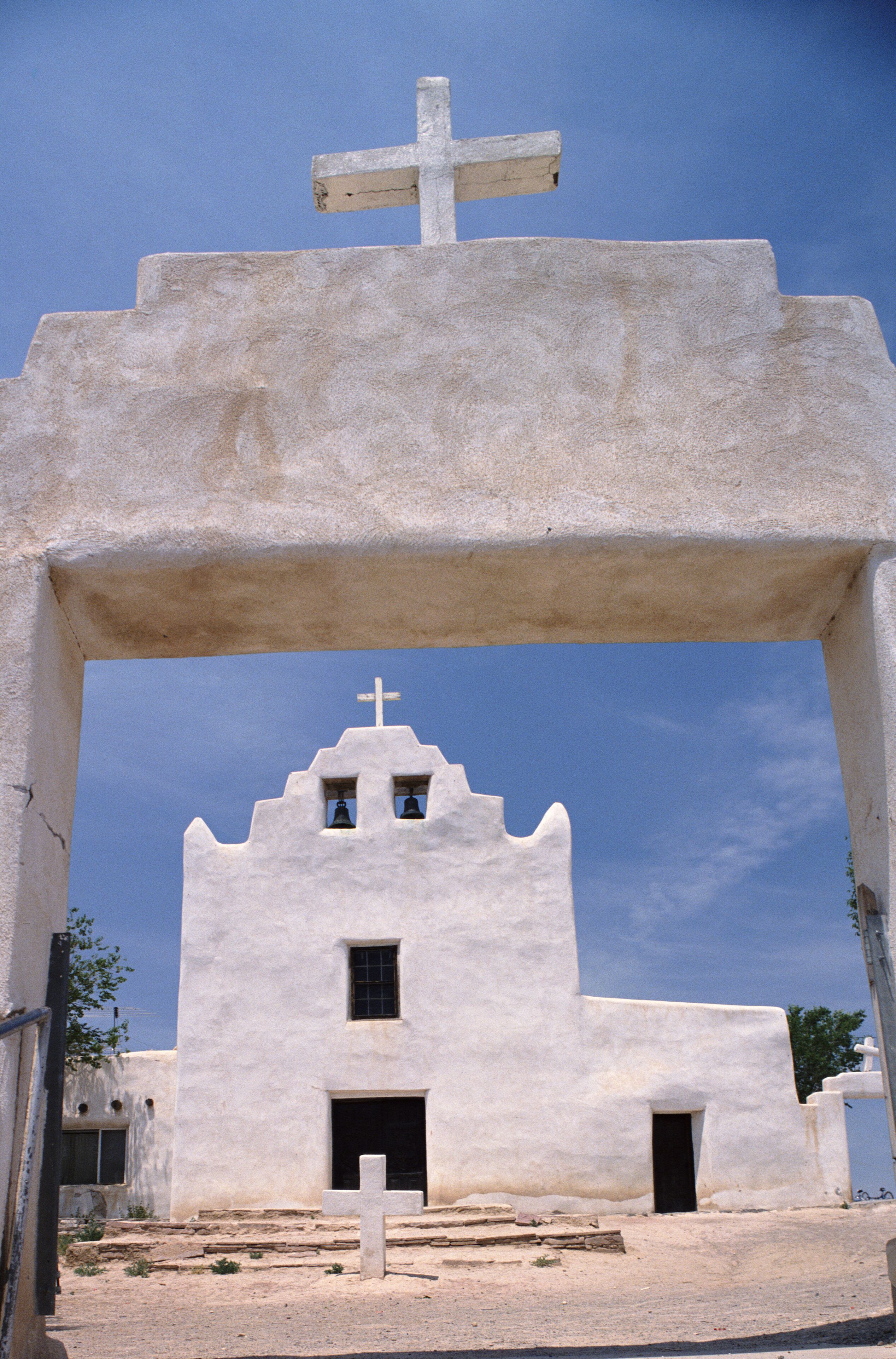 A white church with a cross on top, a bell tower, and a doorway.