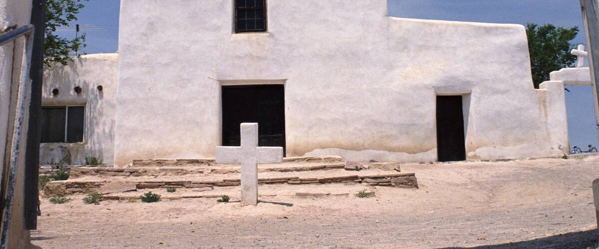 A white church with a cross on top, a bell tower, and a doorway.