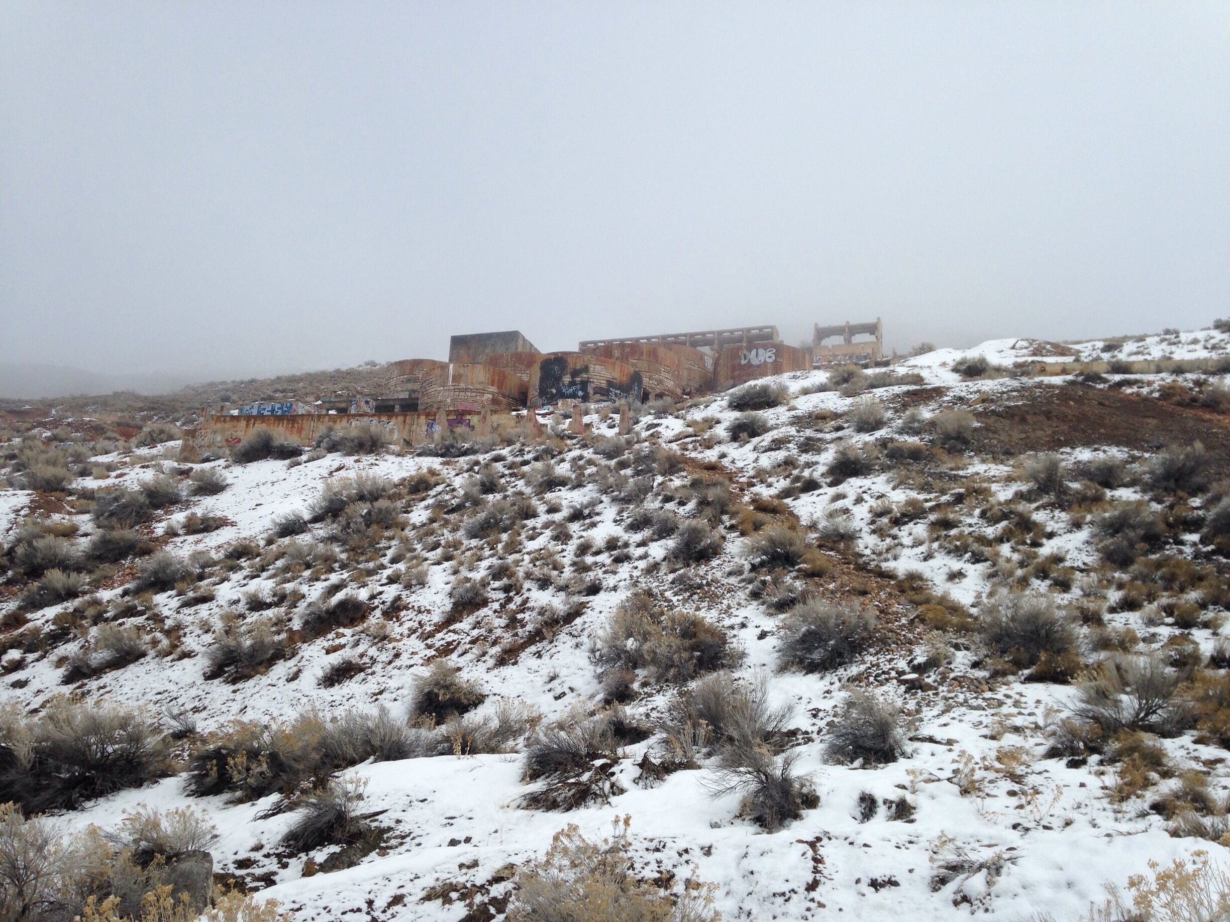 A snow-covered landscape with a rusted train car and graffiti on a hill.