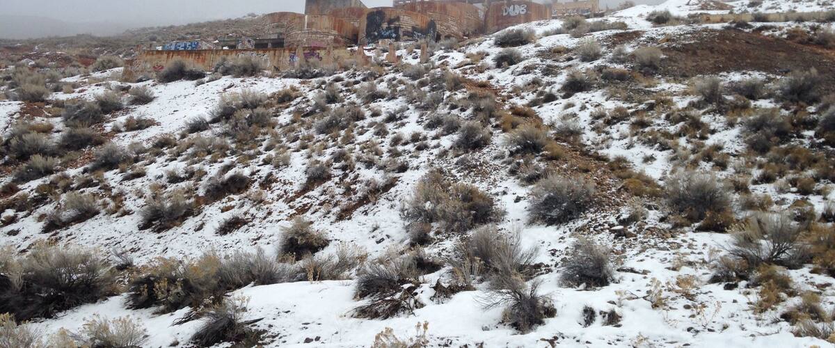 A snow-covered landscape with a rusted train car and graffiti on a hill.