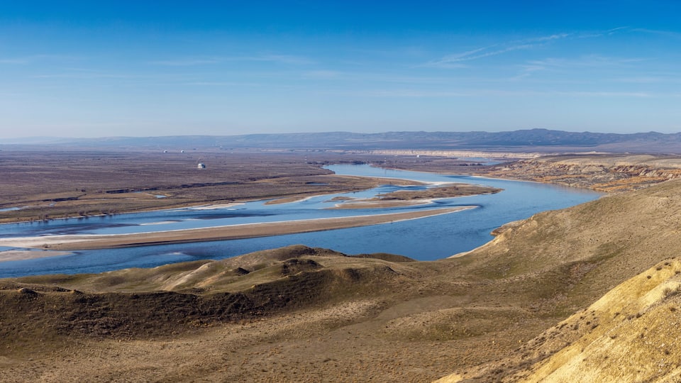 A river winding through a dry, hilly landscape with distant mountains under a clear sky.