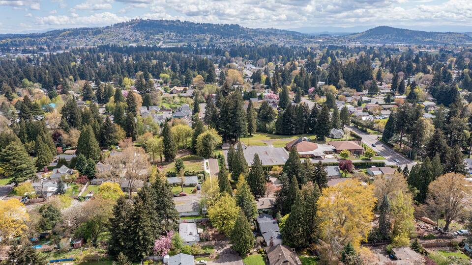 Aerial drone view of Milwaukie, OR, showcasing residential neighborhoods, tree-lined streets, and urban landscape along the Willamette River, with views of parks, commercial areas, and suburban homes
