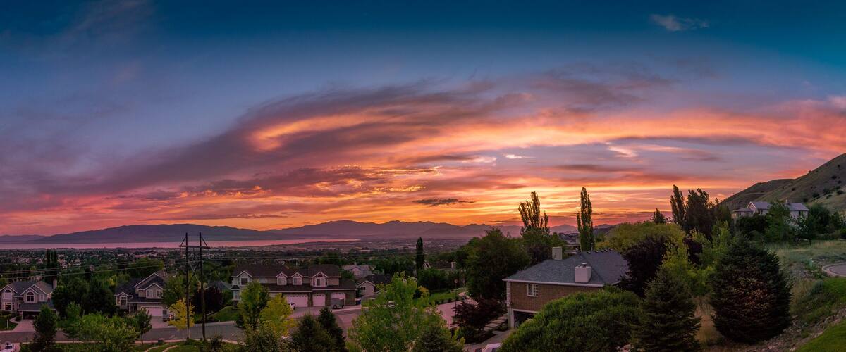 A suburban landscape with houses, a winding road, and a mountainous backdrop during sunset.