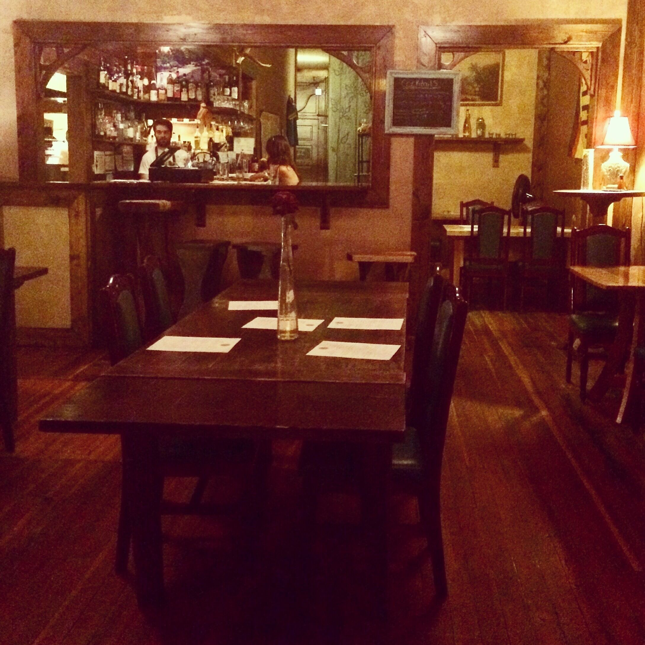 A dimly lit restaurant with wooden furniture and a bar in the background.
