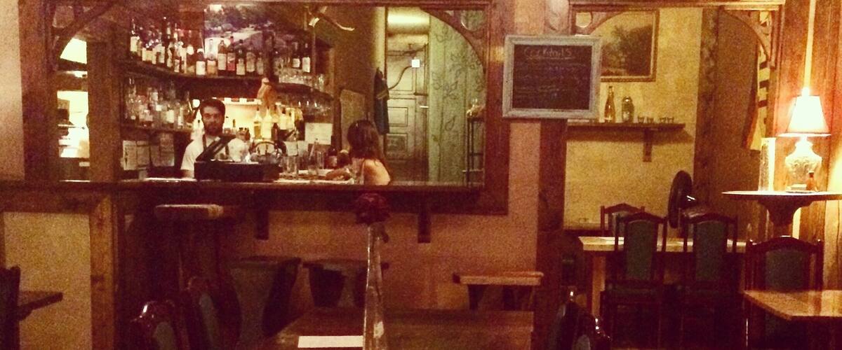A dimly lit restaurant with wooden furniture and a bar in the background.