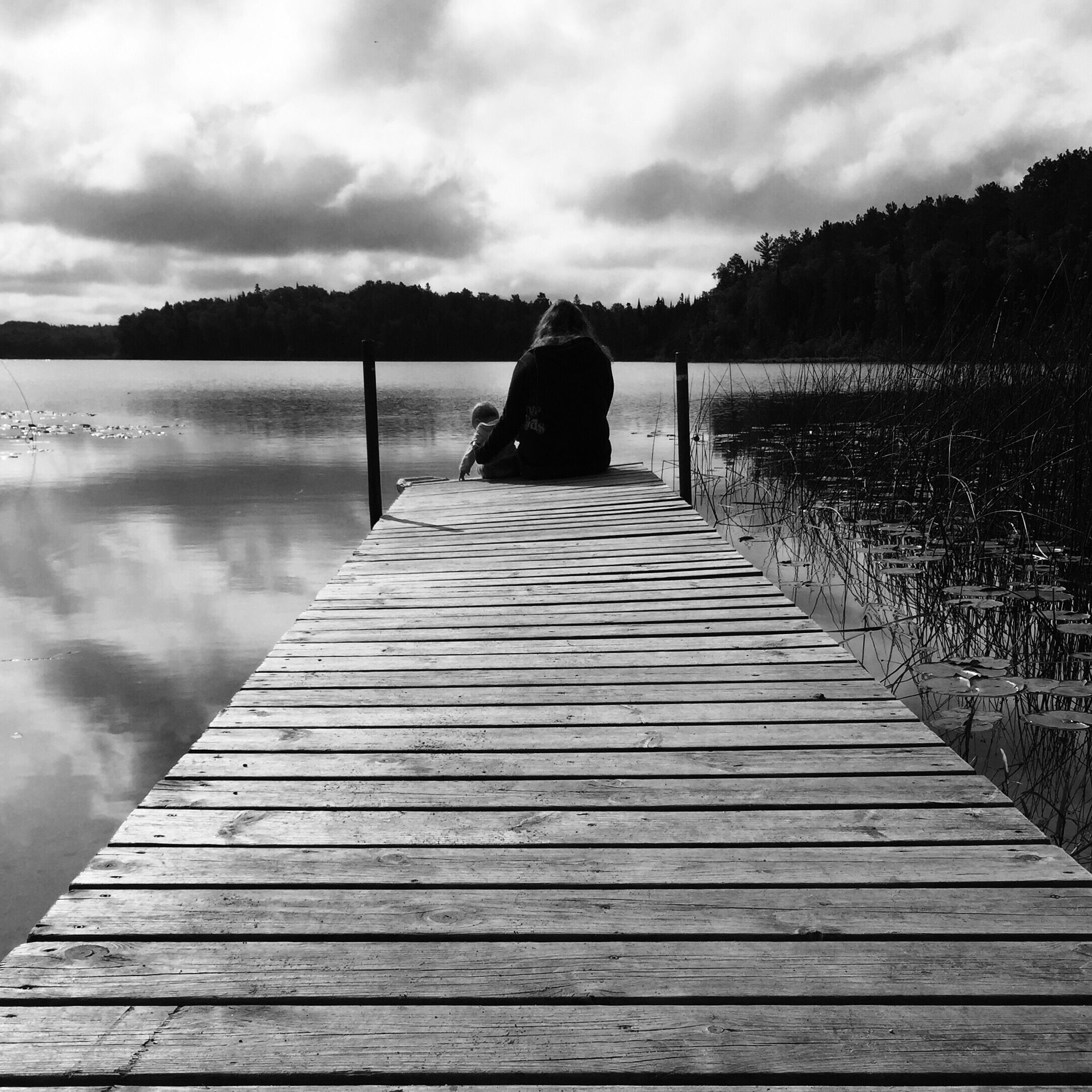 A wooden pier extending into calm water, with a person sitting at the end.