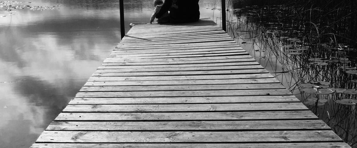 A wooden pier extending into calm water, with a person sitting at the end.