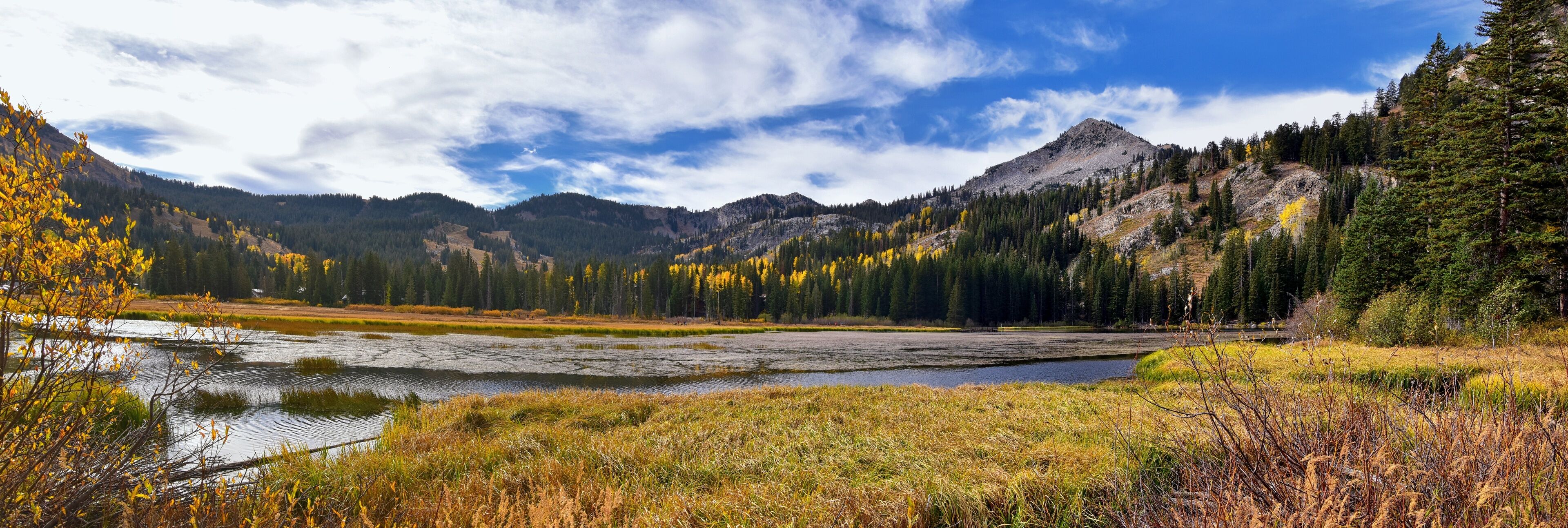A mountainous landscape with a lake, autumn-colored trees, and a clear sky.