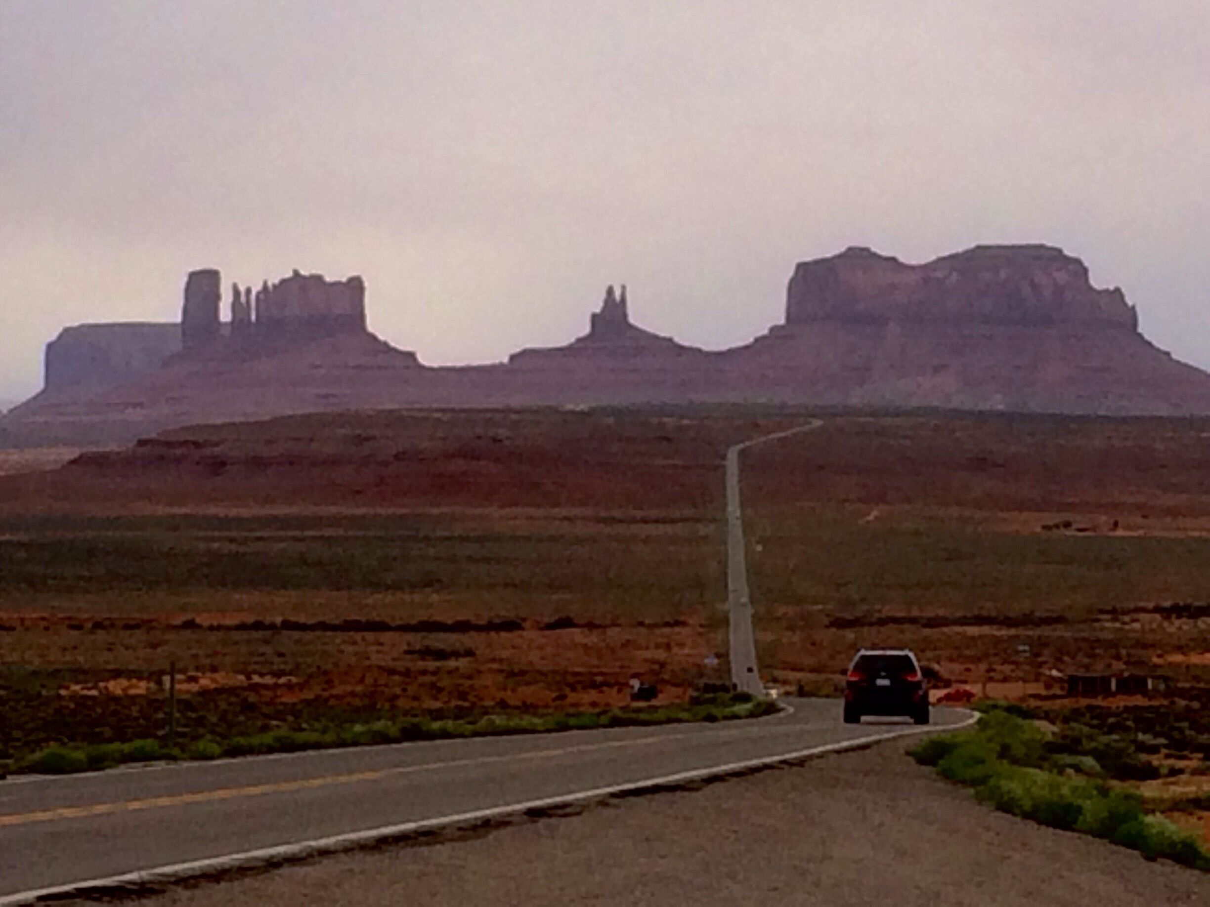 A road leading to a large rock formation with a car approaching.