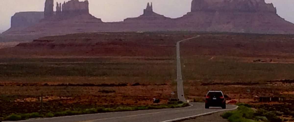 A road leading to a large rock formation with a car approaching.