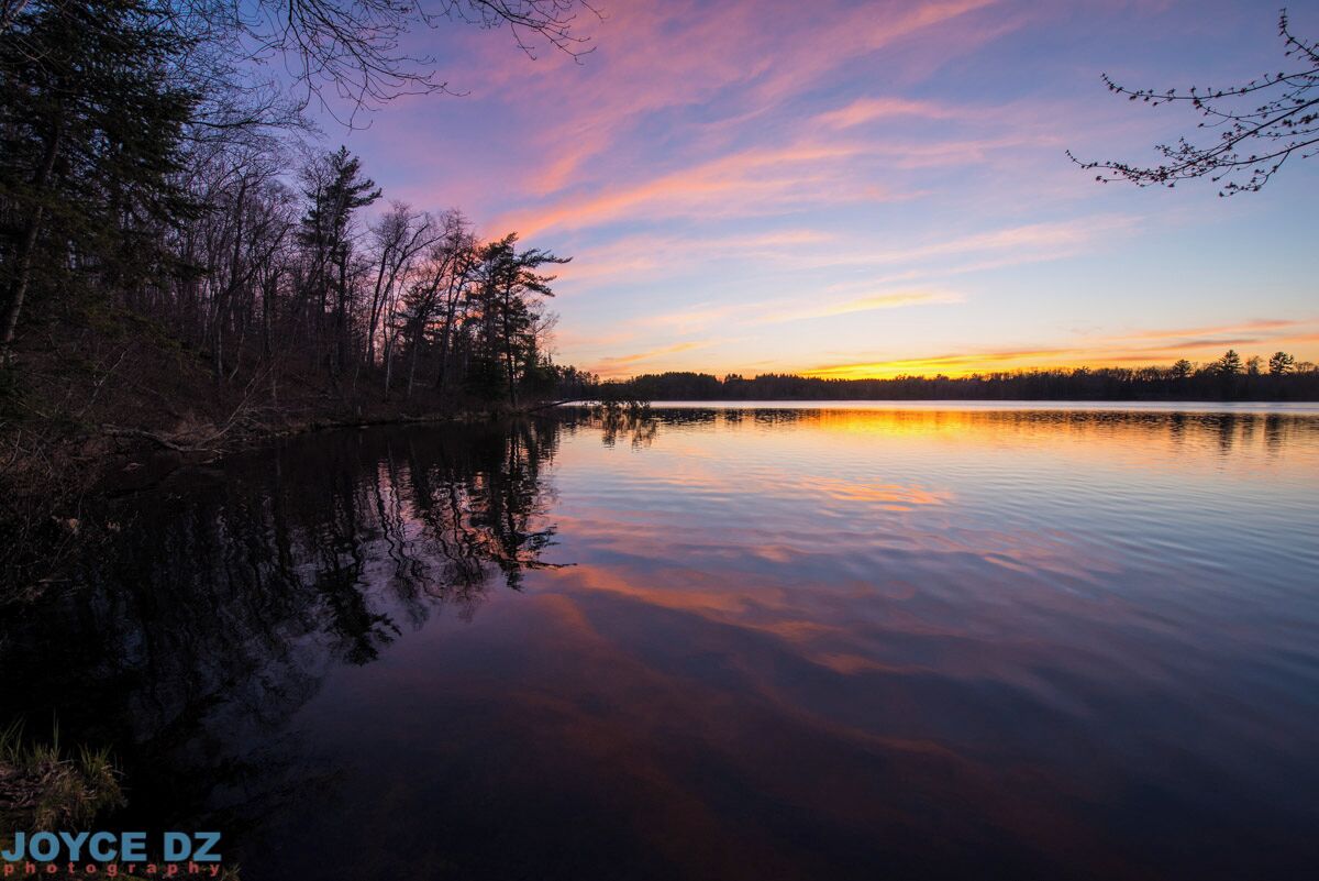 A calm lake at sunset with trees reflecting the sky.