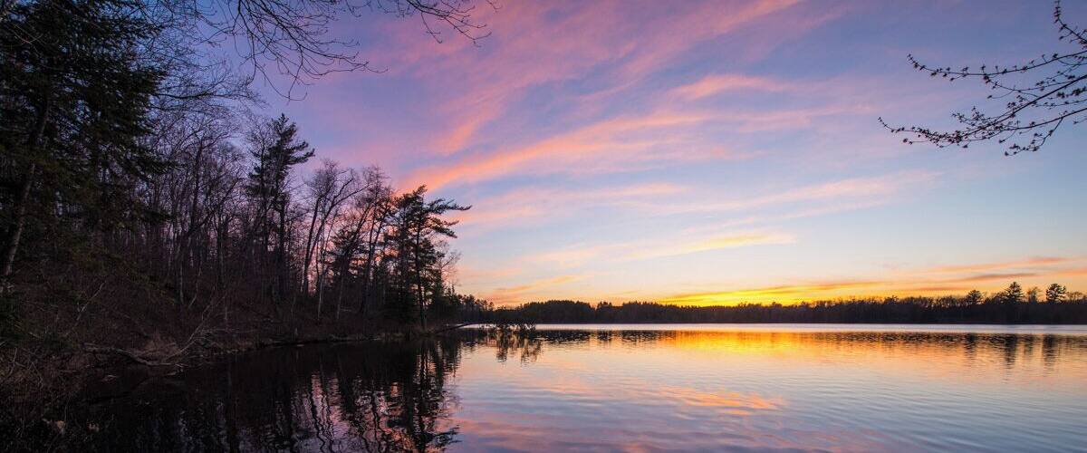 A calm lake at sunset with trees reflecting the sky.