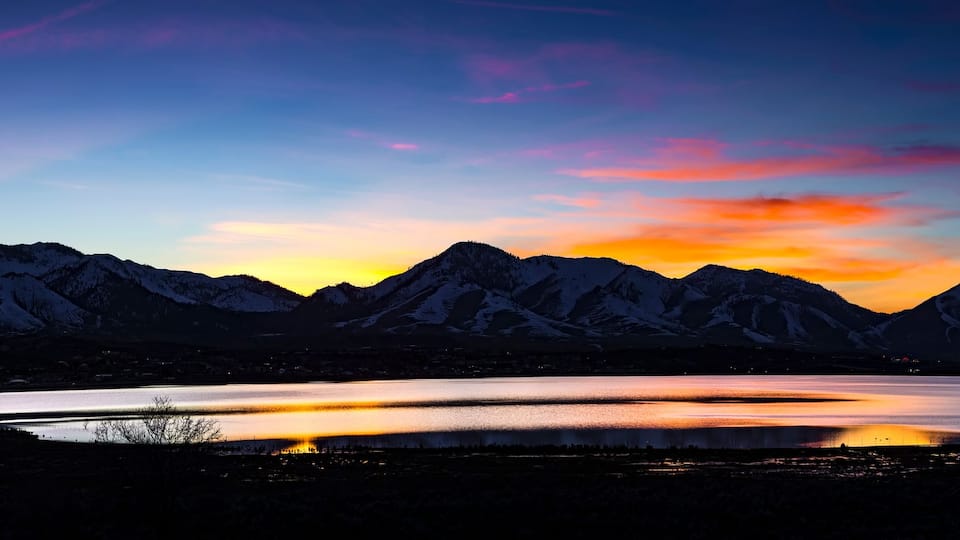 A mountain range at sunset with a lake in the foreground.