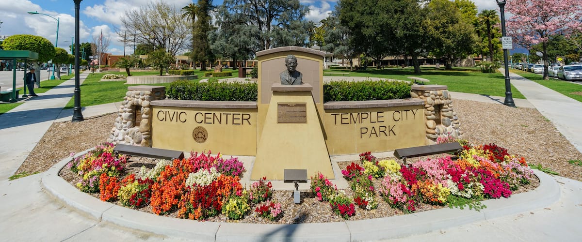 A park with a central monument, flower beds, and a clear blue sky.
