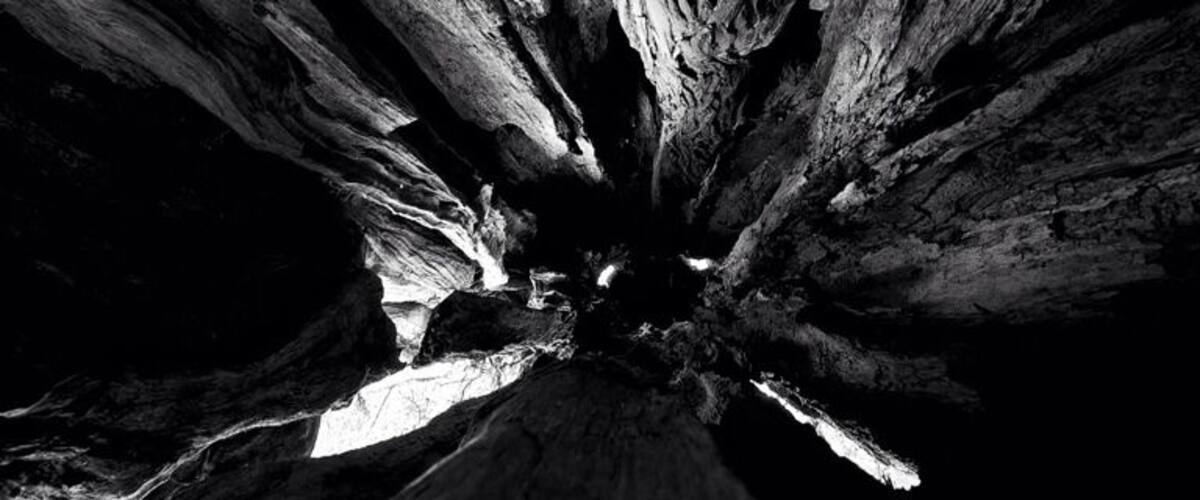 A black and white view of a rock formation with layered strata converging towards a central point.