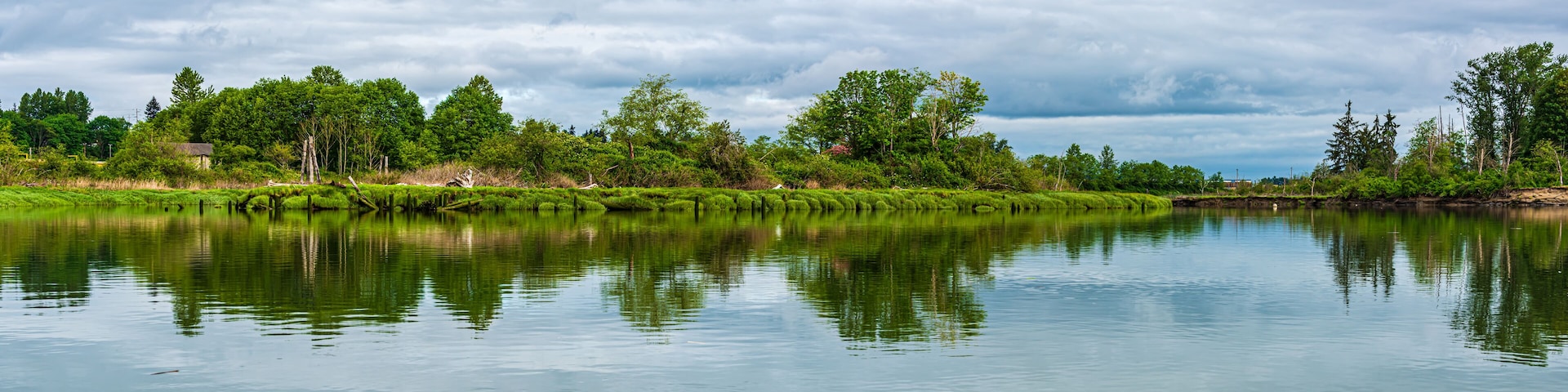 A calm river reflecting trees and a cloudy sky.