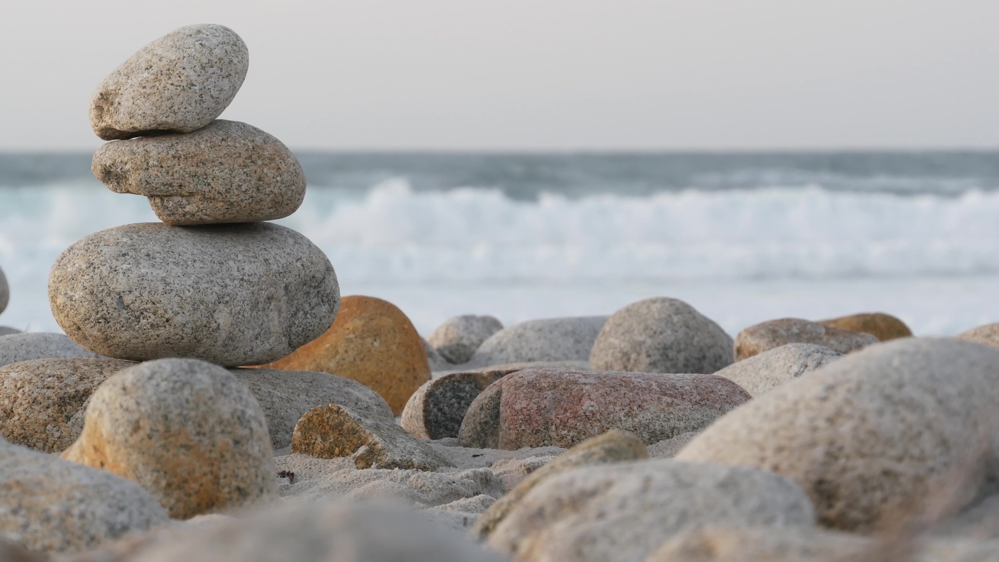 A stack of smooth, rounded stones on a pebbly beach with waves in the background.