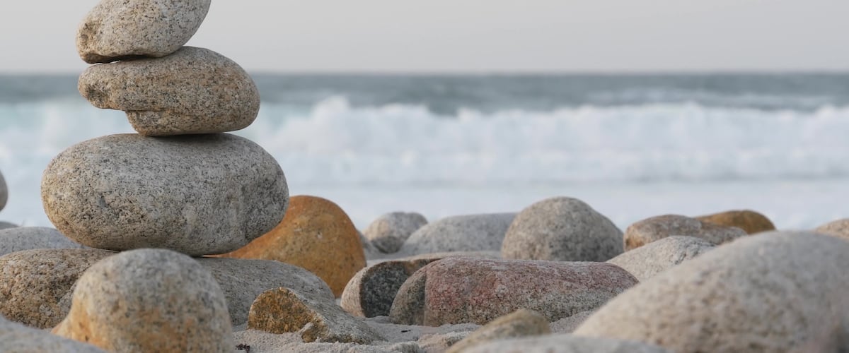 A stack of smooth, rounded stones on a pebbly beach with waves in the background.